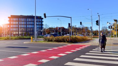 Varşova, Polonya. 5 Kasım 2024. Caddeden karşıya geçen kaldırımda yürüyen yaşlı bir kadın. Sokaktaki son sınıf öğrencisi..