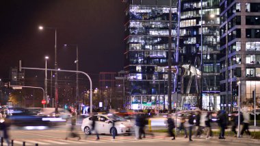 Varşova, Polonya. 21 Kasım 2024. Geceleri sokakta arabaların sokak fotoğrafçılığı. Modern binanın arka planındaki ışık izleri.