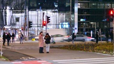 Varşova, Polonya. 21 Kasım 2024. Geceleri sokakta arabaların sokak fotoğrafçılığı. Modern binanın arka planındaki ışık izleri.