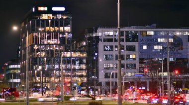 Varşova, Polonya. 21 Kasım 2024. Geceleri sokakta arabaların sokak fotoğrafçılığı. Modern binanın arka planındaki ışık izleri.