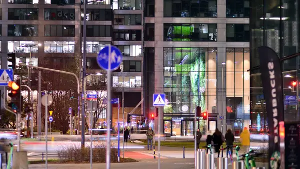 Varşova, Polonya. 21 Kasım 2024. Geceleri sokakta arabaların sokak fotoğrafçılığı. Modern binanın arka planındaki ışık izleri.