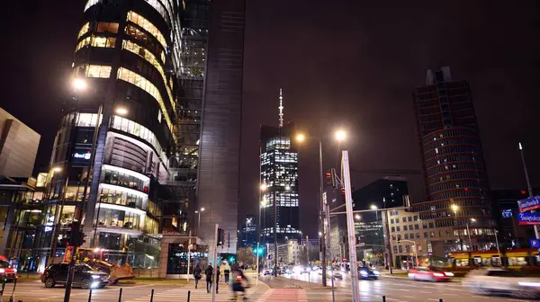 Varşova, Polonya. 21 Kasım 2024. Geceleri sokakta arabaların sokak fotoğrafçılığı. Modern binanın arka planındaki ışık izleri.