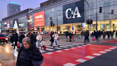 Varşova, Polonya. 22 Kasım 2024. Büyük bir şehrin caddesi. Farklı yaşlarda insanlar karşıdan karşıya geçiyor. Şehir caddesi manzarası sakinleri, turistler ve modern binalar. Şehir merkezinde bir akşam.