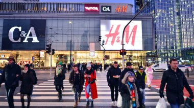 Varşova, Polonya. 22 Kasım 2024. Büyük bir şehrin caddesi. Farklı yaşlarda insanlar karşıdan karşıya geçiyor. Şehir caddesi manzarası sakinleri, turistler ve modern binalar. Şehir merkezinde bir akşam.