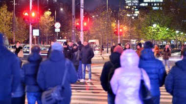 Varşova, Polonya. 22 Kasım 2024. Büyük bir şehrin caddesi. Farklı yaşlarda insanlar karşıdan karşıya geçiyor. Şehir caddesi manzarası sakinleri, turistler ve modern binalar. Şehir merkezinde bir akşam.