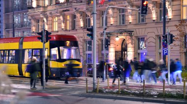 Varşova, Polonya. 22 Kasım 2024. Büyük bir şehrin caddesi. Farklı yaşlarda insanlar karşıdan karşıya geçiyor. Şehir caddesi manzarası sakinleri, turistler ve modern binalar. Şehir merkezinde bir akşam.
