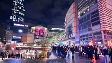 Varşova, Polonya. 22 Kasım 2024. Geceleri sokaktaki insanların sokak fotoğrafçılığı. Modern binanın arka planındaki yaya siluetleri. İnsanların hareket bulanıklığı. Şehir hayatı kavramı.