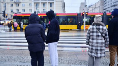 Varşova, Polonya. 12 Ocak 2025. Farklı yaşlarda insanlar karşıdan karşıya geçiyor. Büyük bir şehrin kış caddesi. Şehir caddesi manzarası sakinleri, turistler ve modern binalar.  