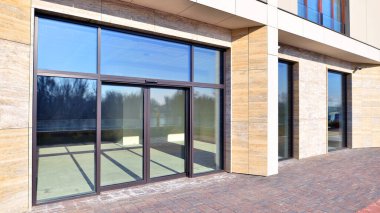 Çok aydınlık bir günde geniş cam cepheli modern bir ticari bina manzarası. Kiralanmayı bekleyen yeni ticari öneri.