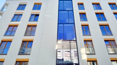 Şehirde simetrik modern mimarisi olan bir apartman. Güneşli bir günde modern apartman binası. Modern bir apartmanın ön cephesi. Alt görünüm. 