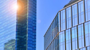 Şehir merkezindeki işletme bölgesi mimarisi. Mavi gökyüzüne ve güneş ışığına karşı cam yansıtıcı ofis binaları. Ekonomi, finans, iş faaliyeti konsepti. Ufukta yükselen güneş.