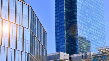 Şehir merkezindeki işletme bölgesi mimarisi. Mavi gökyüzüne ve güneş ışığına karşı cam yansıtıcı ofis binaları. Ekonomi, finans, iş faaliyeti konsepti. Ufukta yükselen güneş.