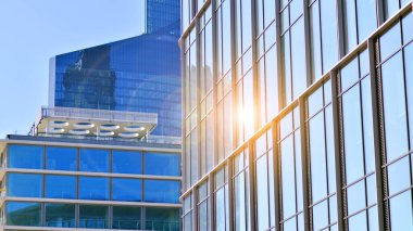 Şehir merkezindeki işletme bölgesi mimarisi. Mavi gökyüzüne ve güneş ışığına karşı cam yansıtıcı ofis binaları. Ekonomi, finans, iş faaliyeti konsepti. Ufukta yükselen güneş.