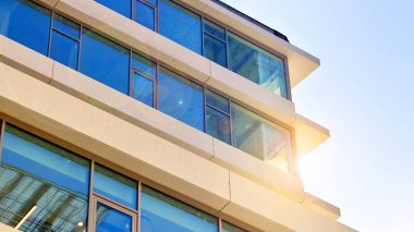 Şehir merkezindeki işletme bölgesi mimarisi. Mavi gökyüzüne ve güneş ışığına karşı cam yansıtıcı ofis binaları. Ekonomi, finans, iş faaliyeti konsepti. Ufukta yükselen güneş.