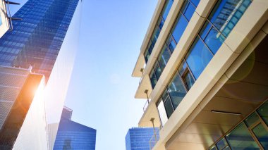 Şehir merkezindeki işletme bölgesi mimarisi. Mavi gökyüzüne ve güneş ışığına karşı cam yansıtıcı ofis binaları. Ekonomi, finans, iş faaliyeti konsepti. Ufukta yükselen güneş.