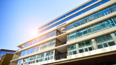 Şehir merkezindeki işletme bölgesi mimarisi. Mavi gökyüzüne ve güneş ışığına karşı cam yansıtıcı ofis binaları. Ekonomi, finans, iş faaliyeti konsepti. Ufukta yükselen güneş.