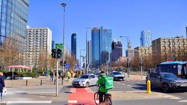 Varşova, Polonya. 28 Mart 2025. Büyük bir şehrin caddesi. Farklı yaşlarda insanlar karşıdan karşıya geçiyor. Şehir caddesi manzarası sakinleri, turistler ve modern binalar. Şehir merkezinde güneşli bir günde.