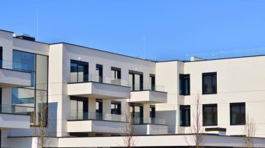 Güneşli bir günde kentsel konut binalarının modern mimarisi. Büyük pencereleri ve geniş terasları olan düşük katlı apartmanlar. Modern bir apartmanın beyaz cephesi.