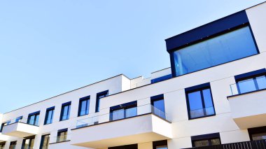 Güneşli bir günde kentsel konut binalarının modern mimarisi. Büyük pencereleri ve geniş terasları olan düşük katlı apartmanlar. Modern bir apartmanın beyaz cephesi.