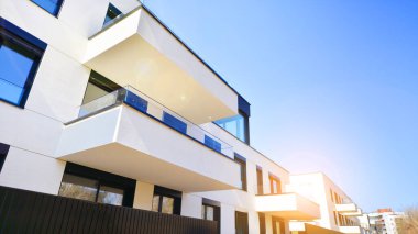 Güneşli bir günde kentsel konut binalarının modern mimarisi. Büyük pencereleri ve geniş terasları olan düşük katlı apartmanlar. Modern bir apartmanın beyaz cephesi.