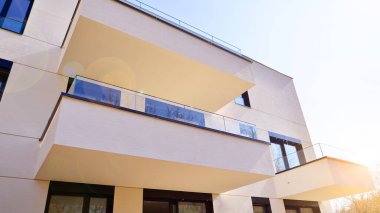 Güneşli bir günde kentsel konut binalarının modern mimarisi. Büyük pencereleri ve geniş terasları olan düşük katlı apartmanlar. Modern bir apartmanın beyaz cephesi.