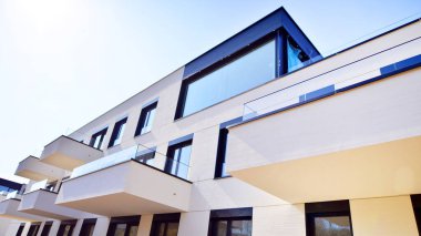Güneşli bir günde kentsel konut binalarının modern mimarisi. Büyük pencereleri ve geniş terasları olan düşük katlı apartmanlar. Modern bir apartmanın beyaz cephesi.