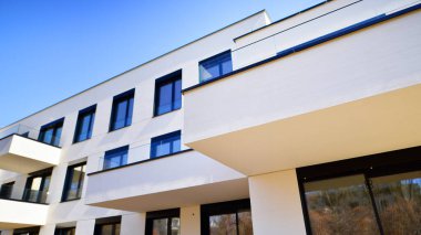 Güneşli bir günde kentsel konut binalarının modern mimarisi. Büyük pencereleri ve geniş terasları olan düşük katlı apartmanlar. Modern bir apartmanın beyaz cephesi.