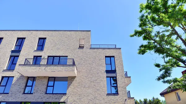 Çevre mimarisi. Yeşil ağaç ve yeni konut binası. Doğanın ve modernliğin ahengi. Yeşil yerleşim bölgesinde yeni daireleri olan modern bir apartman..