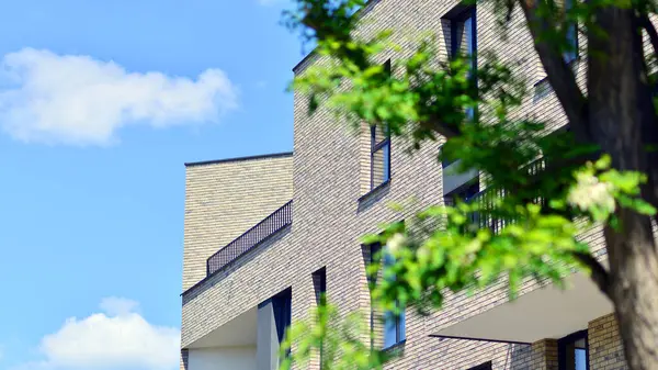 Çevre mimarisi. Yeşil ağaç ve yeni konut binası. Doğanın ve modernliğin ahengi. Yeşil yerleşim bölgesinde yeni daireleri olan modern bir apartman..