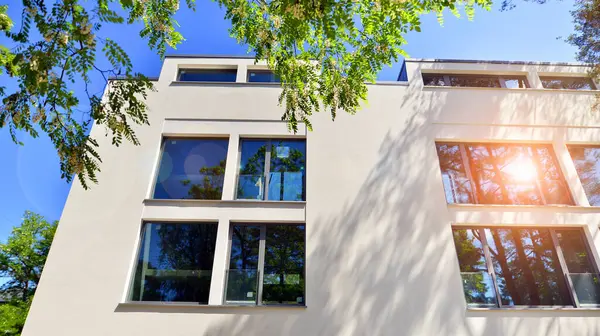 Çevre mimarisi. Yeşil ağaç ve yeni konut binası. Doğanın ve modernliğin ahengi. Yeşil yerleşim bölgesinde yeni daireleri olan modern bir apartman..