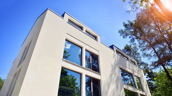 Çevre mimarisi. Yeşil ağaç ve yeni konut binası. Doğanın ve modernliğin ahengi. Yeşil yerleşim bölgesinde yeni daireleri olan modern bir apartman..