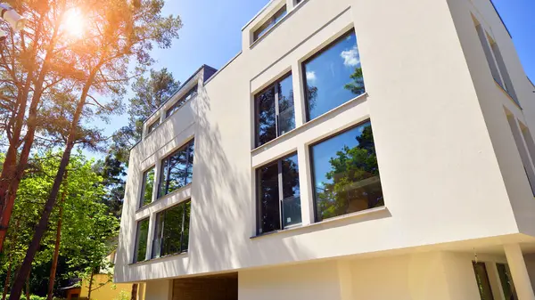 Çevre mimarisi. Yeşil ağaç ve yeni konut binası. Doğanın ve modernliğin ahengi. Yeşil yerleşim bölgesinde yeni daireleri olan modern bir apartman..