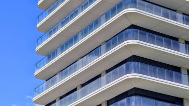 Çok katlı, modern bir apartmanın dış cephesi, pencereleri ve balkonları. Modern cam balkon parmaklıkları.