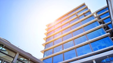 Cam cepheli modern ofis binası. Ofis binasının şeffaf cam duvarı. Binanın ön cephesinde mavi gökyüzünün yansıması.