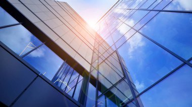 Cam cepheli modern ofis binası. Ofis binasının şeffaf cam duvarı. Binanın ön cephesinde mavi gökyüzünün yansıması.