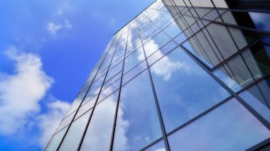 Cam cepheli modern ofis binası. Ofis binasının şeffaf cam duvarı. Binanın ön cephesinde mavi gökyüzünün yansıması.