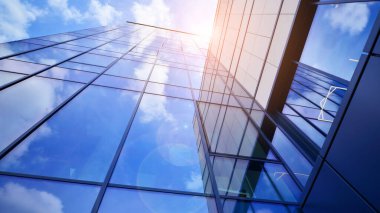 Cam cepheli modern ofis binası. Ofis binasının şeffaf cam duvarı. Binanın ön cephesinde mavi gökyüzünün yansıması.