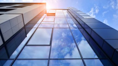 Cam cepheli modern ofis binası. Ofis binasının şeffaf cam duvarı. Binanın ön cephesinde mavi gökyüzünün yansıması.