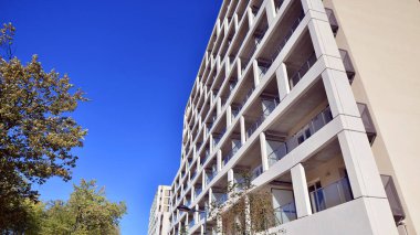 Bereketli yeşil ağaçlarla çevrili ve güneşli bir günde taze bitki örtüsüyle çevrili bir yerleşim yeri. Çağdaş mimari konut kompleksi yeşilliklerle çevrili.