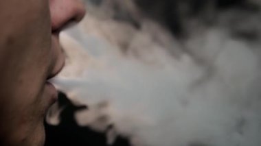 Adam bir sigara tüttürüyor. Siyah bir arkaplana yaklaş. Nikotin bağımlılığı konsepti. Dudaklardan duman çıkar..