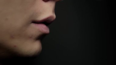 Adam bir sigara tüttürüyor. Siyah bir arkaplana yaklaş. Nikotin bağımlılığı konsepti. Dudaklardan duman çıkar..