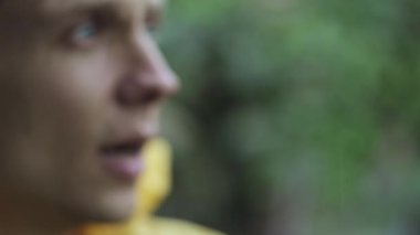 Adam yağmurda sarı yağmurluğu yukarı çeker, ıslak yüzü yakın plan çeker..