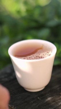Küçük bir çay kasesini almak için uzanan bir elin yakın çekimi..