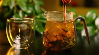 Bir el, cam bir çaydanlıkta çay yapraklarını ahşap bir sopayla karıştırır. Yavaş çekimde sıcak suda büyüleyici bir dans yaratır..