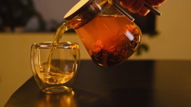 Yeşil yapraklı cam bir fincana sıcak bitki çayı dökülüyor ve soğuk hava için sıcak, sıcak bir atmosfer yaratıyor..