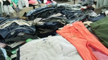 Bir ucuzluk mağazasında farklı renkler ve kumaşlar gösteren bir yığın ikinci el pantolon ve giysi..