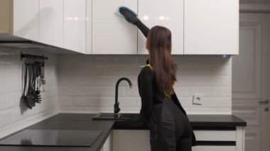 Modern beyaz mutfakta mutfak dolaplarını temizleyen kadın temizleyici. Temizlik hizmetleri