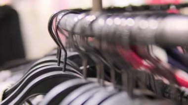 Mağazanın vitrininde elbise askılarının yakın çekimleri moda tercihlerini ve alışveriş deneyimlerini vurguluyor.