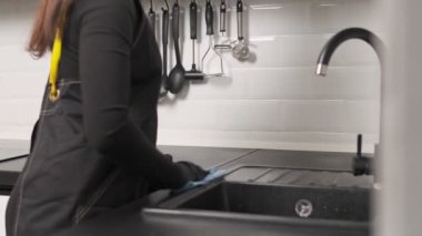 Siyah eldivenli ve önlüklü bir kadın mutfak tezgahını temizliyor..