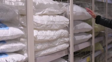 Genç bir kadının bir ev eşyaları mağazasında yastık seçerken, kumaş dokusunu hissederken ve konfor için yumuşaklığı test ederken, kalite ve konfora odaklı detaylı alışveriş deneyimi.